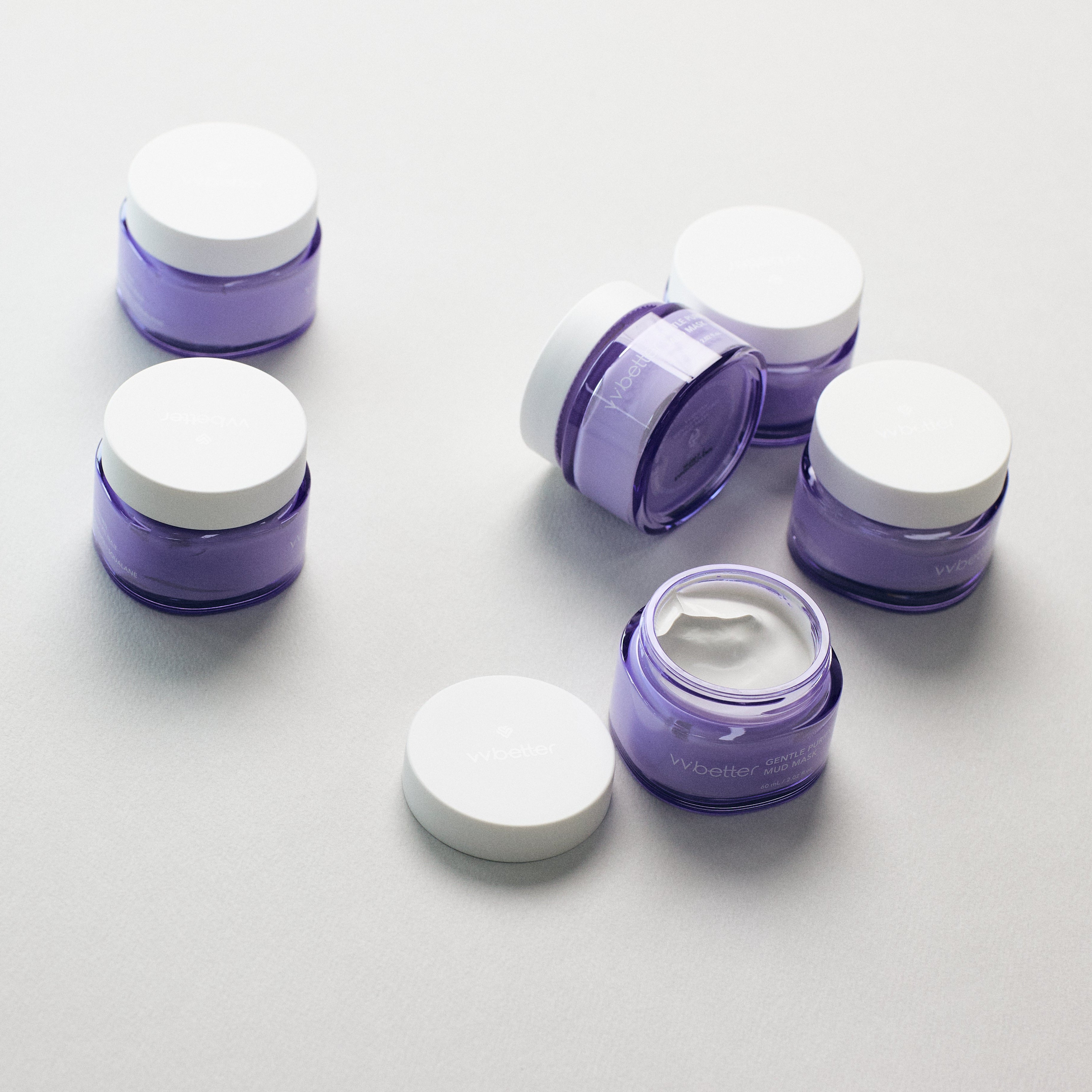 Set of purple skincare containers with white lids on a light gray background